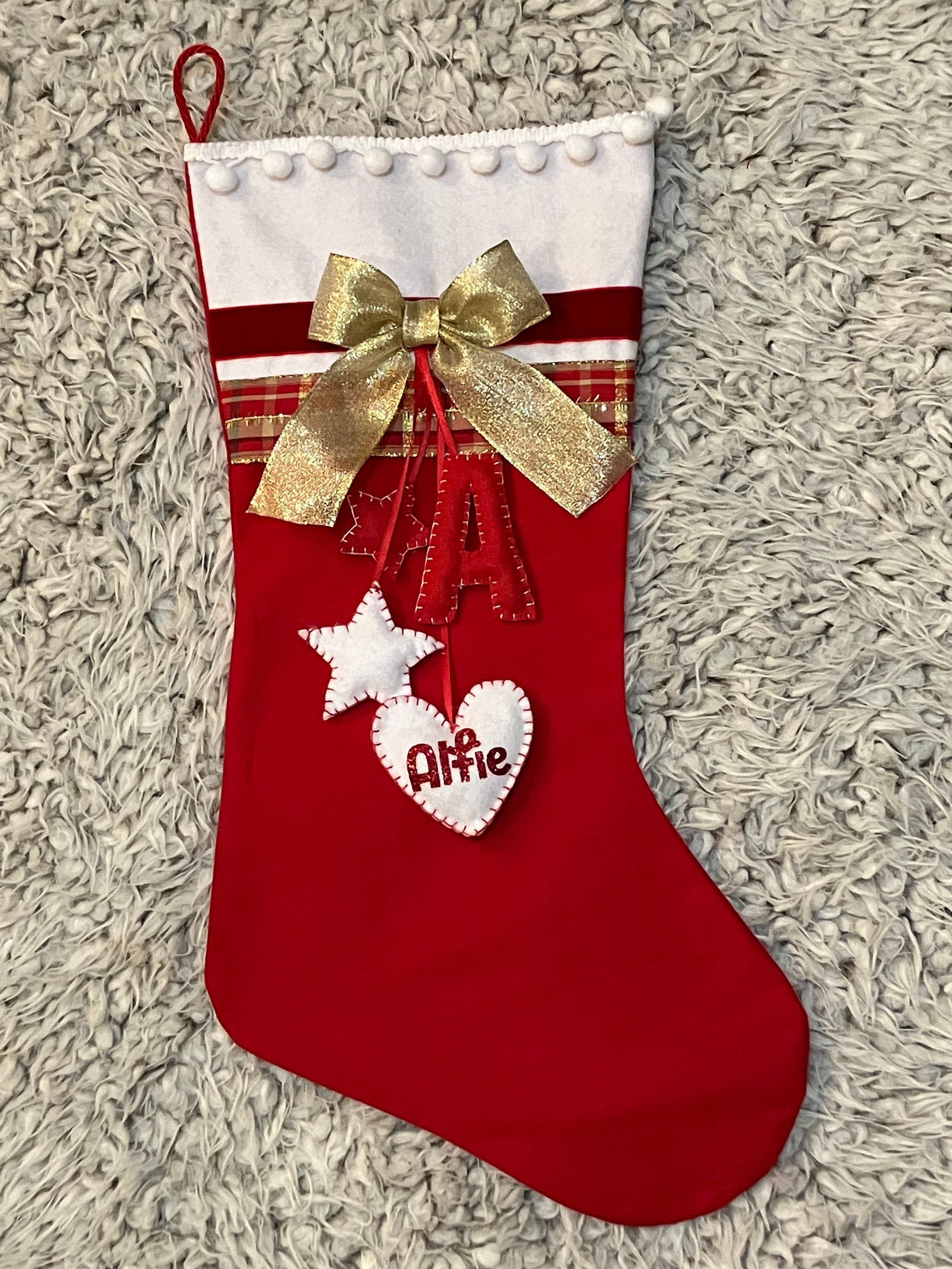 A red Christmas stocking with a gold bow and "Alfie" embroidered on a white heart.