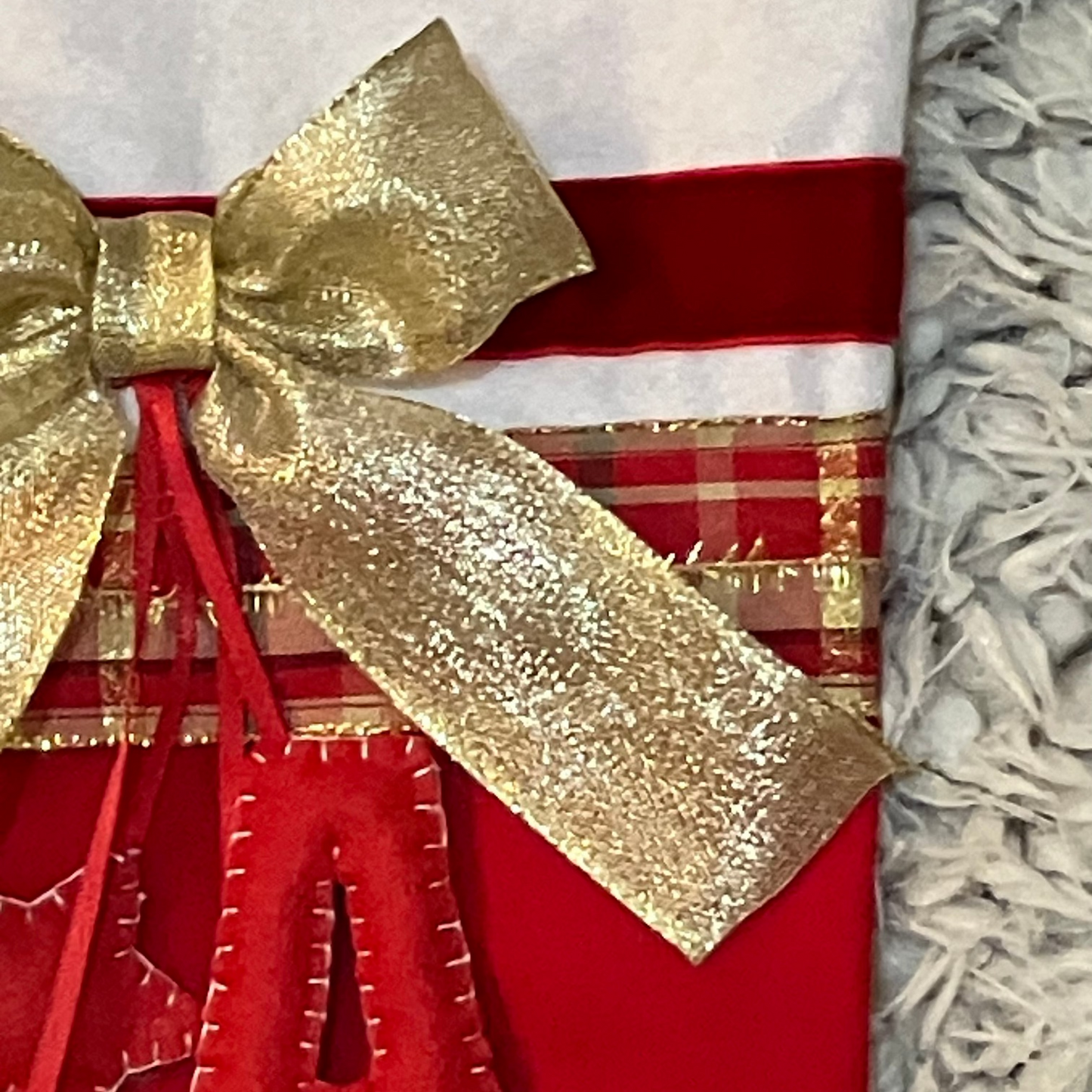 A close-up of a gold glitter bow on a red and plaid Christmas stocking.