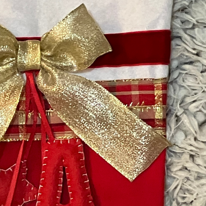 A close-up of a gold glitter bow on a red and plaid Christmas stocking.