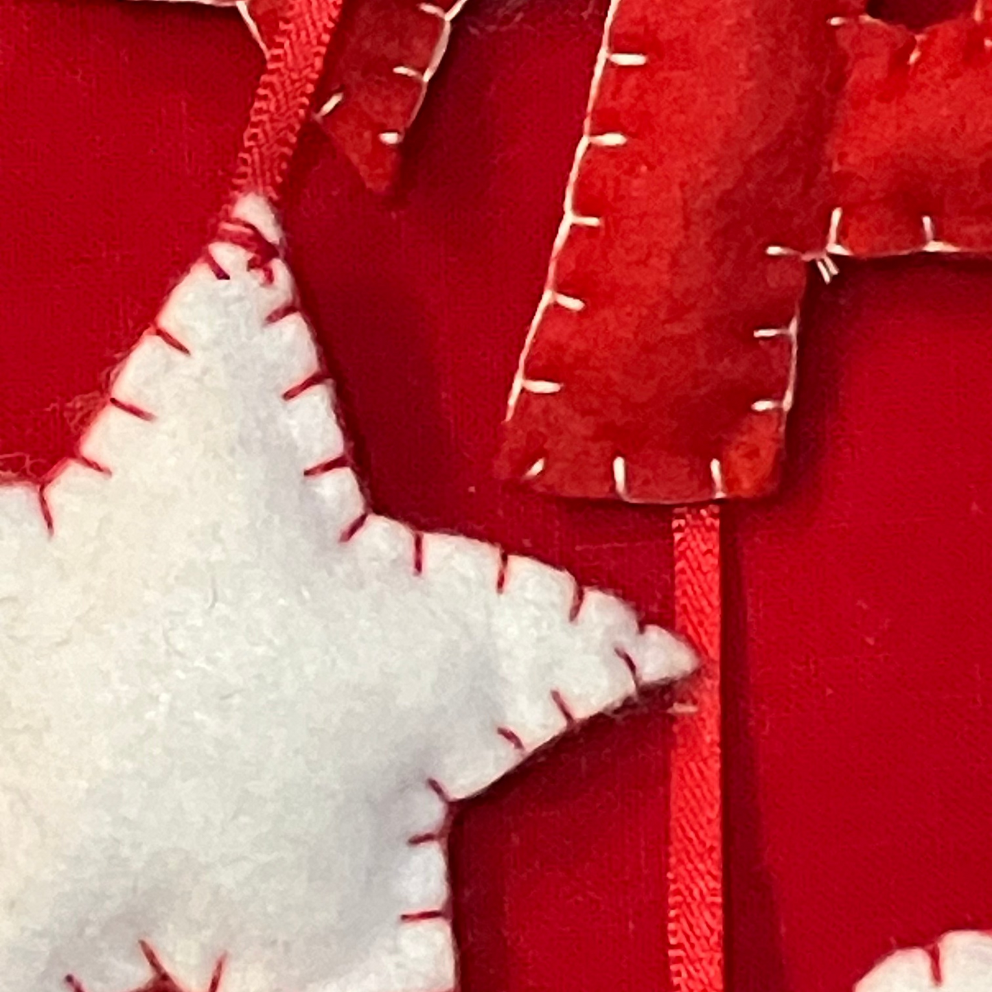 A close-up of red felt letters and a white felt star with red stitching on a red stocking.