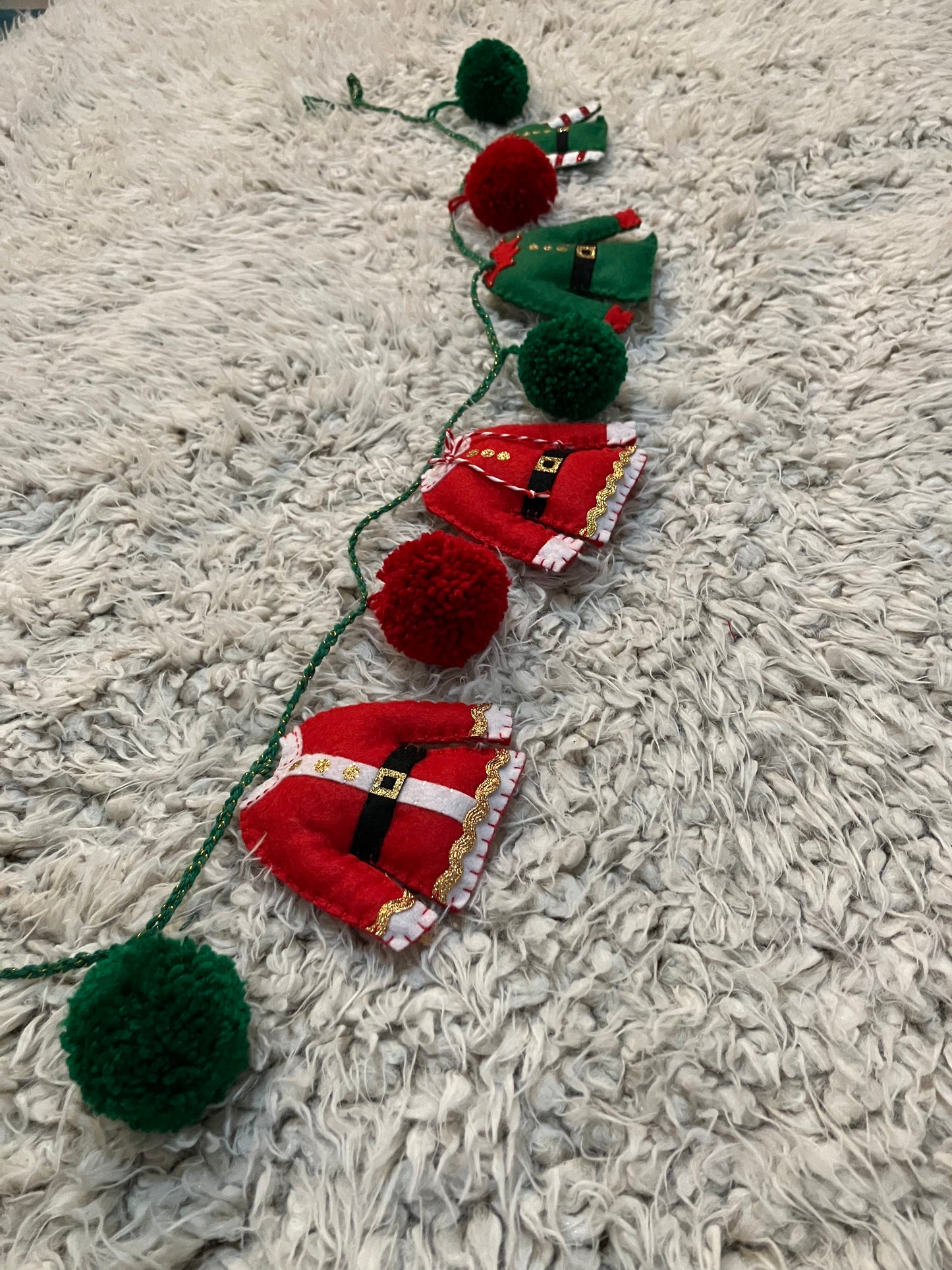 A festive Christmas garland with red and green pom-poms, Santa and elf outfits.