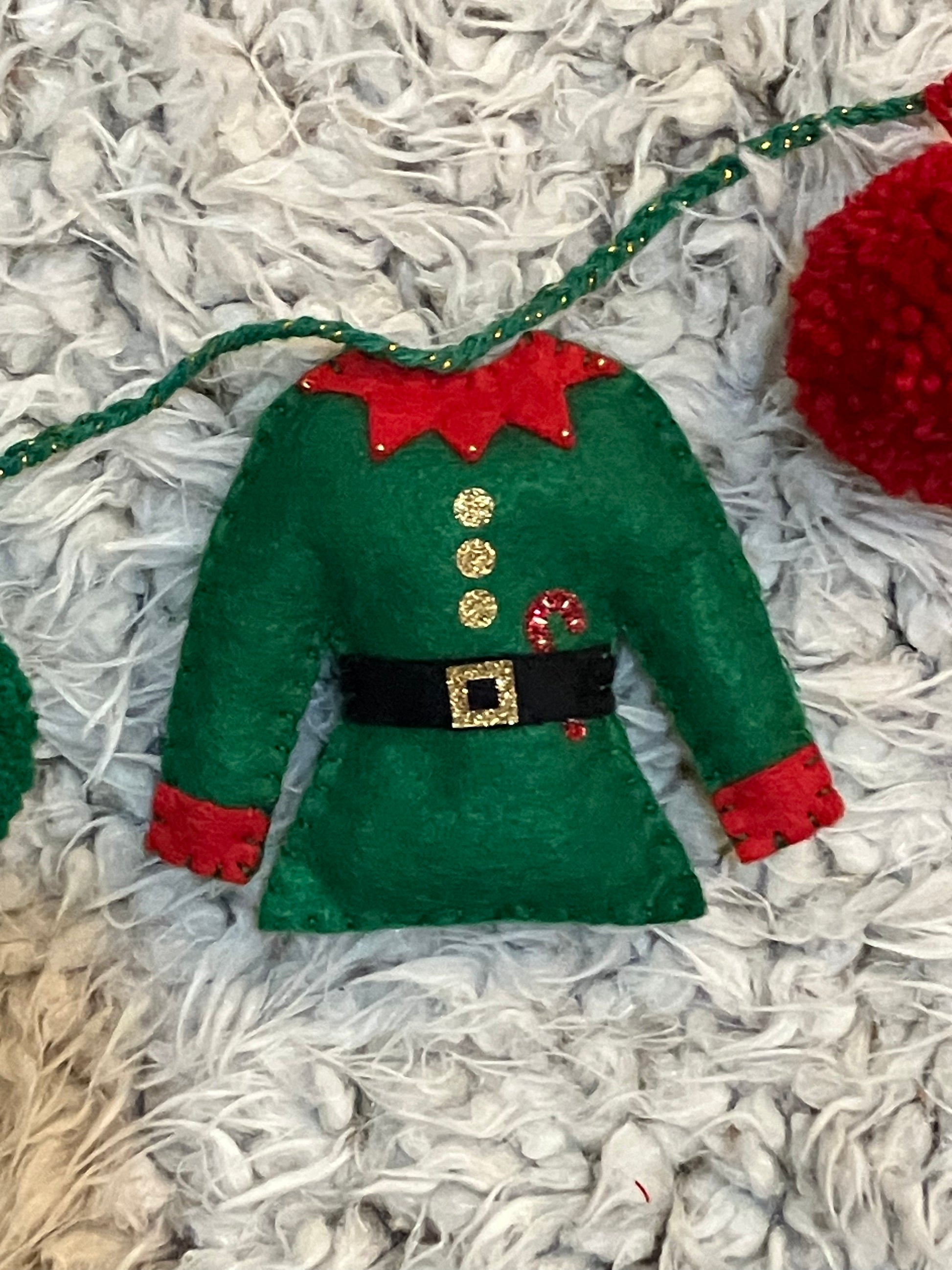 A miniature green elf jacket with a red collar and a small candy cane detail.