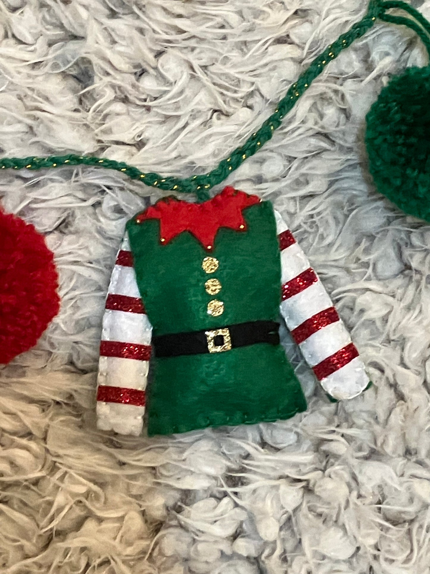 A miniature green elf jacket with red and white striped sleeves and gold buttons.
