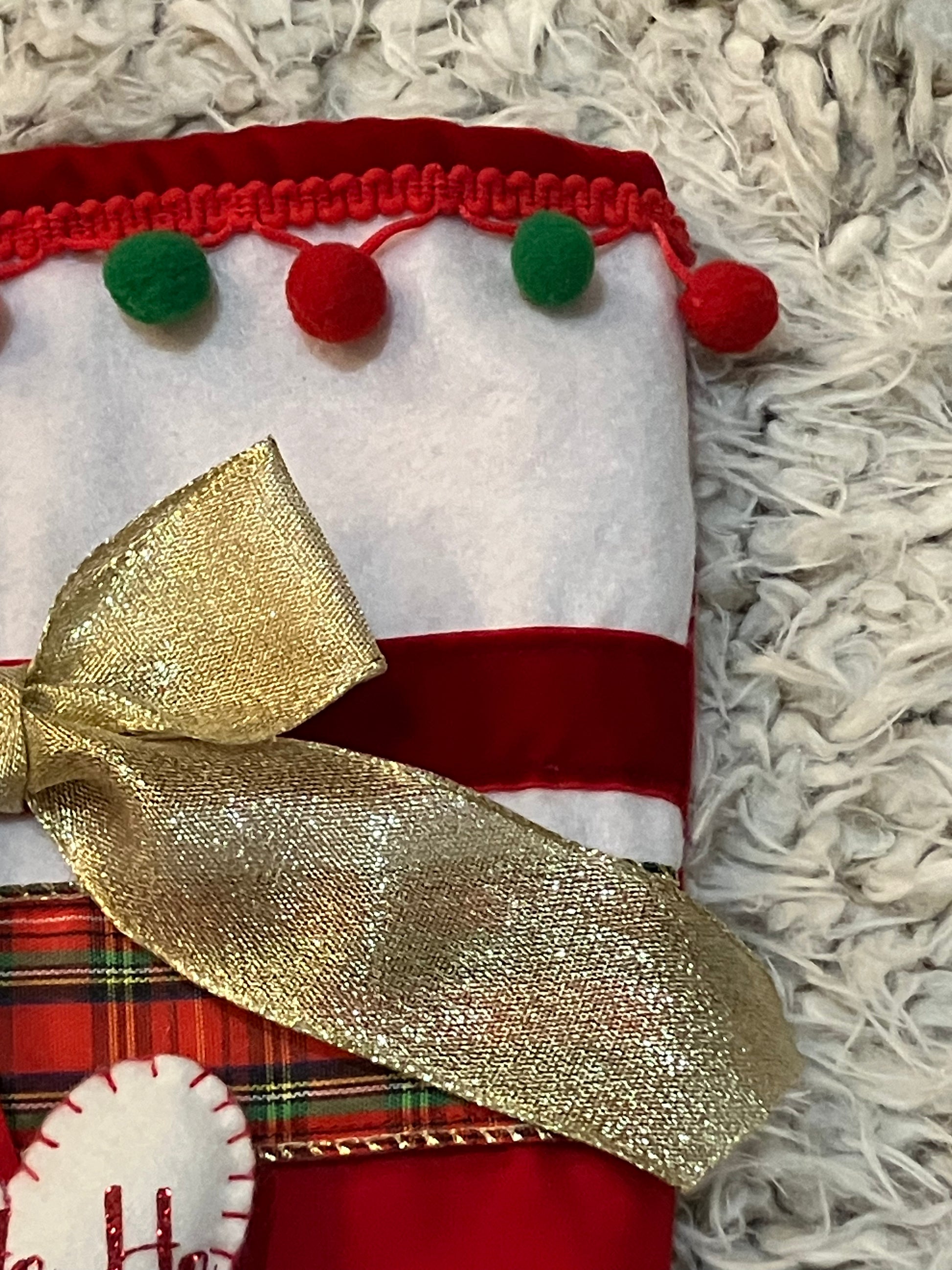 Detail of the top of the Christmas stocking with pom-poms and a gold bow.