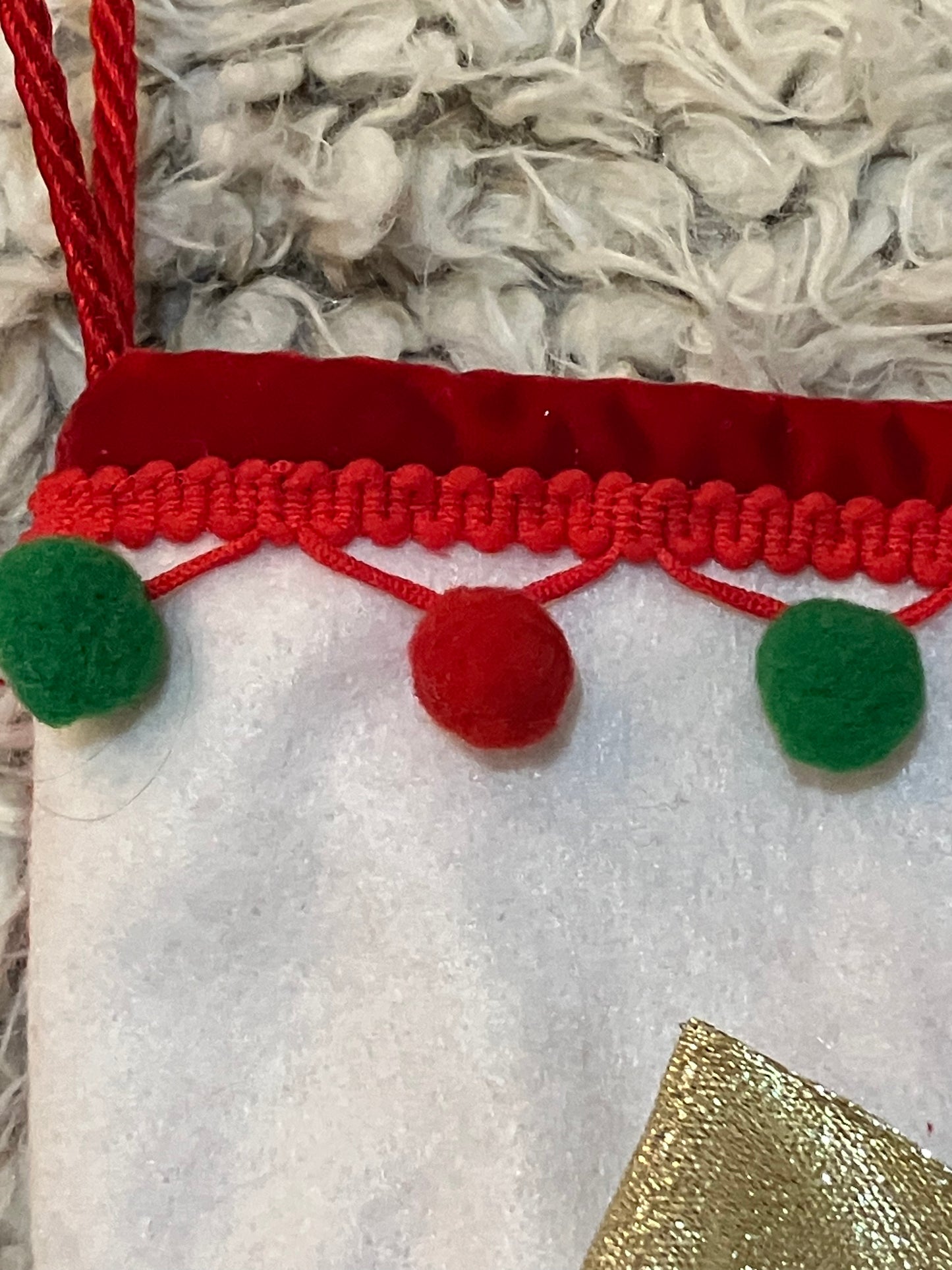 Close-up of the red and green pom-pom trim on the white cuff of the stocking.