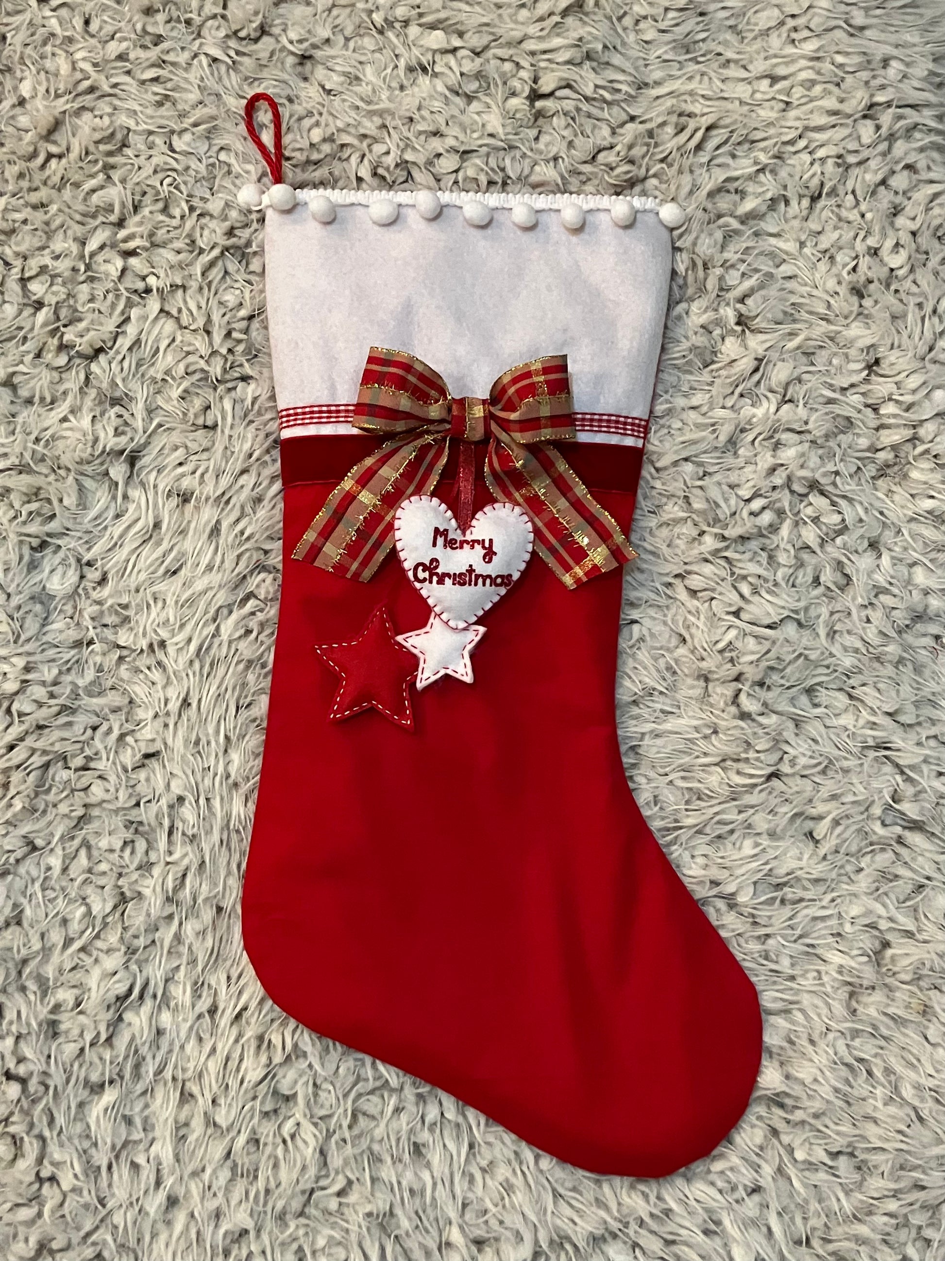 A red Christmas stocking with a plaid bow, felt heart, and two felt stars.