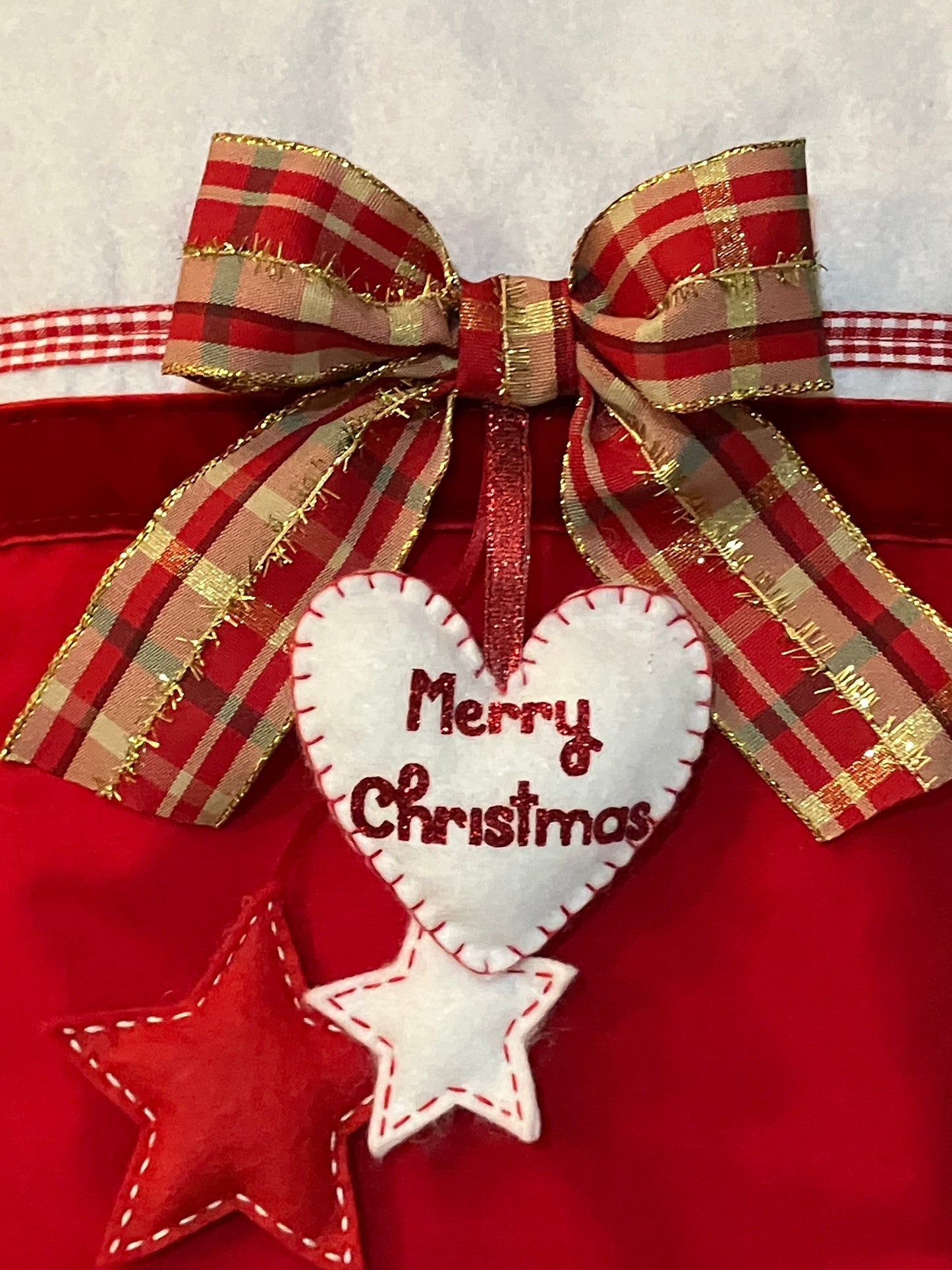 A close-up of a festive red and gold plaid bow, with a white felt heart and two stars.