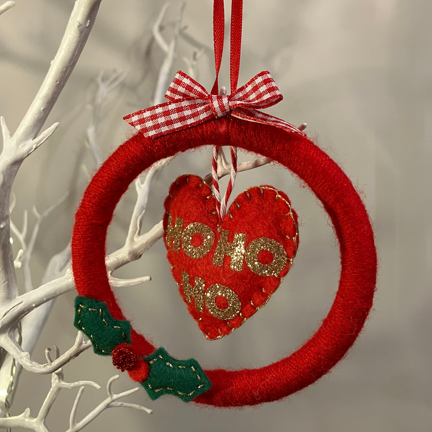 A festive red felt wreath with a 'HO HO HO' heart, hanging from a white branch.