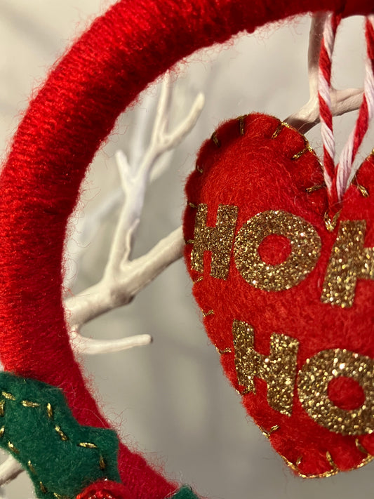 Close-up of the red felt 'HO HO HO' heart ornament with golden glitter text.