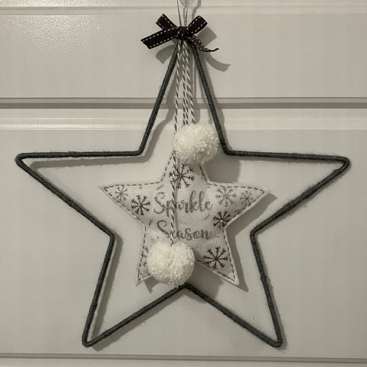 Gray wire star with a fabric star inside that says "Sparkle Season" and two white pom-poms.