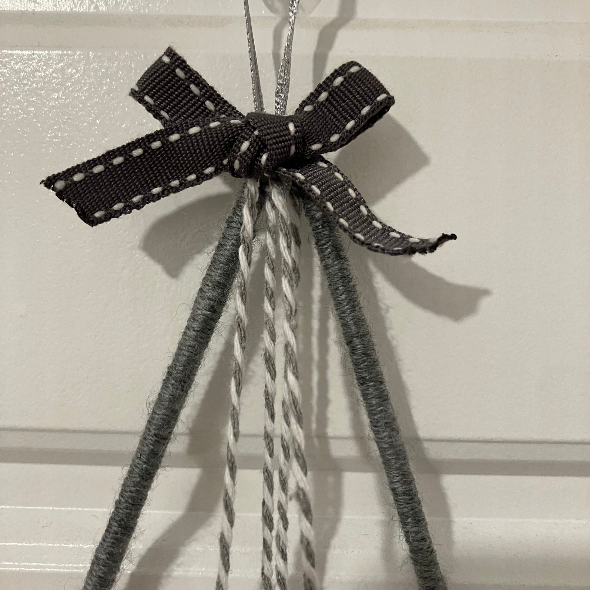 A dark gray ribbon with white stitching tied in a bow, hanging from a hook with gray and white strings.