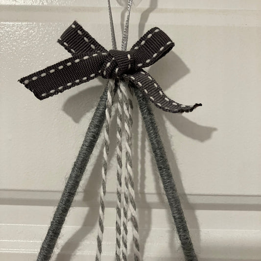 A dark gray ribbon with white stitching tied in a bow, hanging from a hook with gray and white strings.