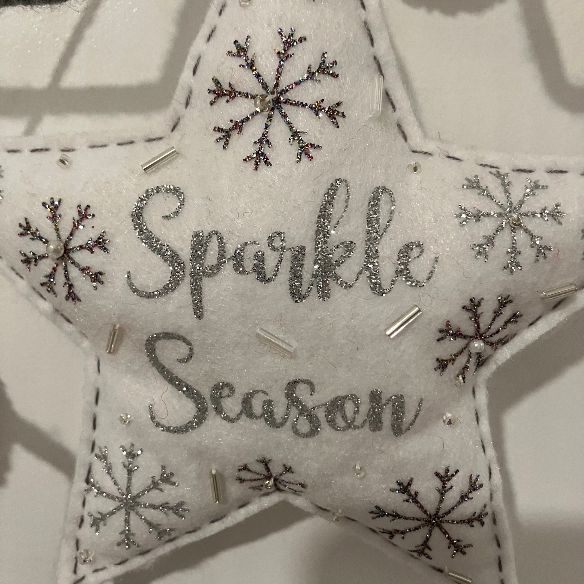 White felt star ornament with "Sparkle Season" in silver glitter and embroidered snowflakes.