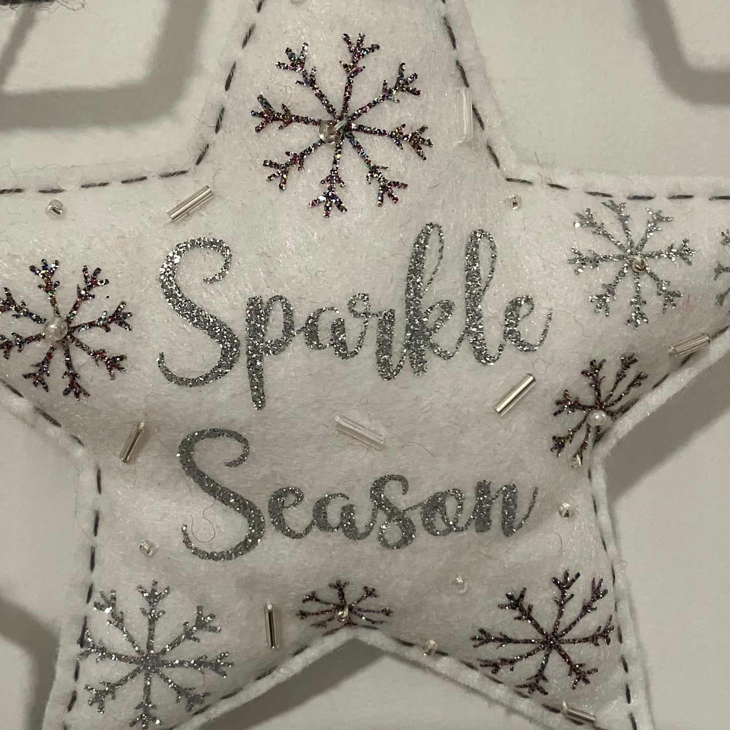 White felt star ornament with "Sparkle Season" in glitter, surrounded by snowflakes and beads.