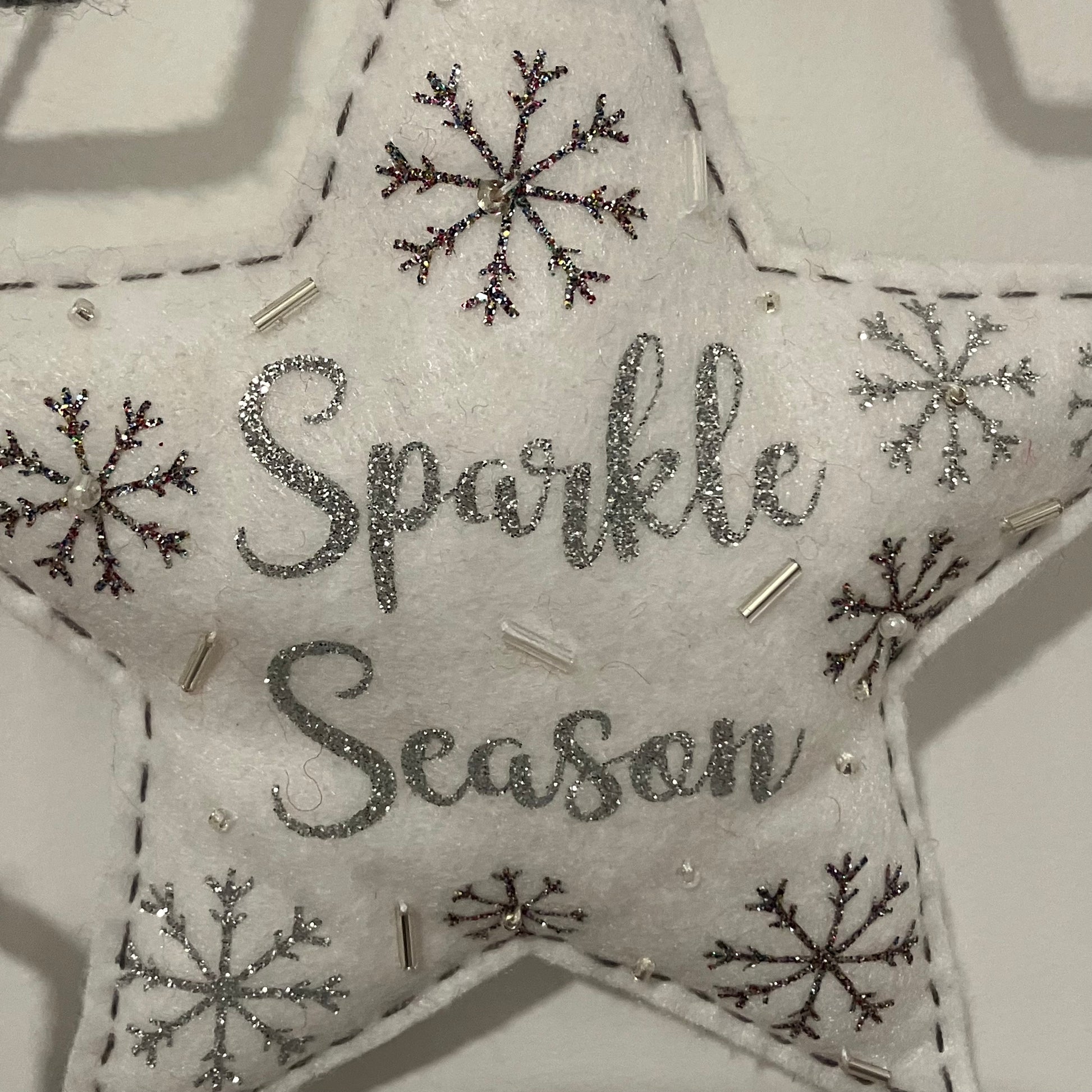 White felt star ornament with "Sparkle Season" in glitter, surrounded by snowflakes and beads.