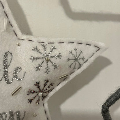 Close-up of a white felt star ornament with silver glitter snowflakes and beads.