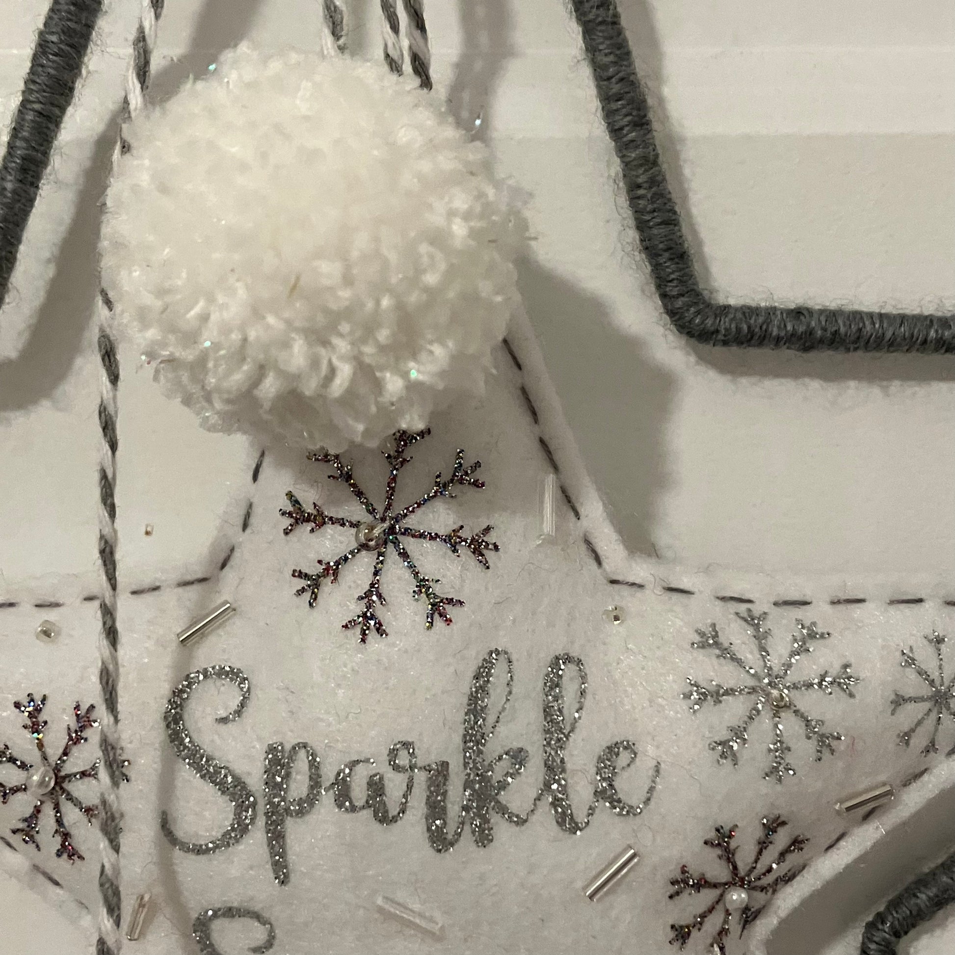 White felt star ornament with "Sparkle" in glitter, snowflakes, beads, and a pom-pom.