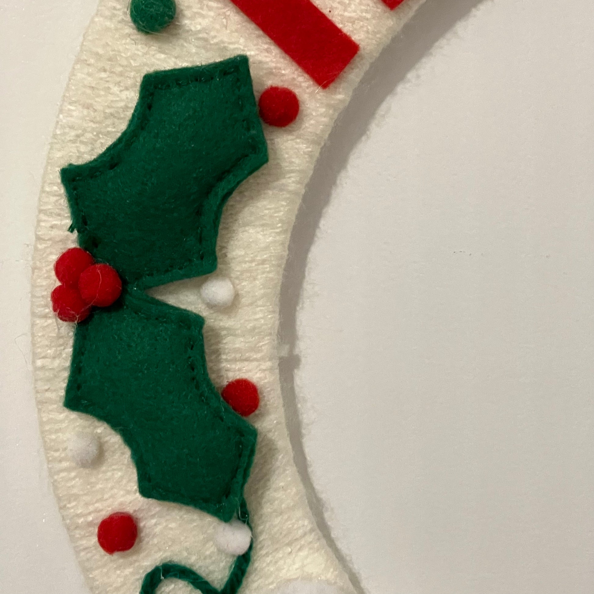 Close-up of a white felt wreath with green holly leaves and red berries.