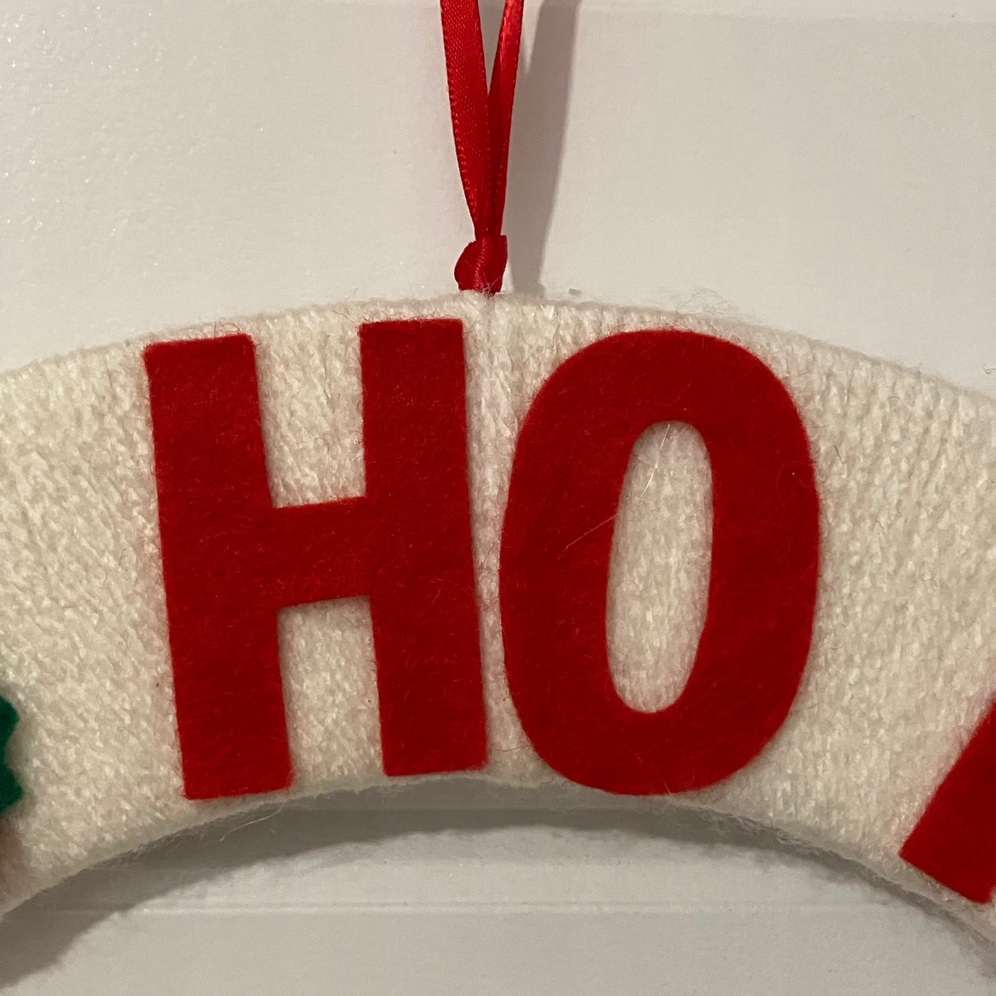 Close-up of a white knitted wreath with red felt letters spelling "HO" and a red ribbon.