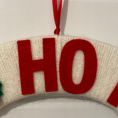 Close-up of a white knitted wreath with red felt letters spelling "HO" and a red ribbon.