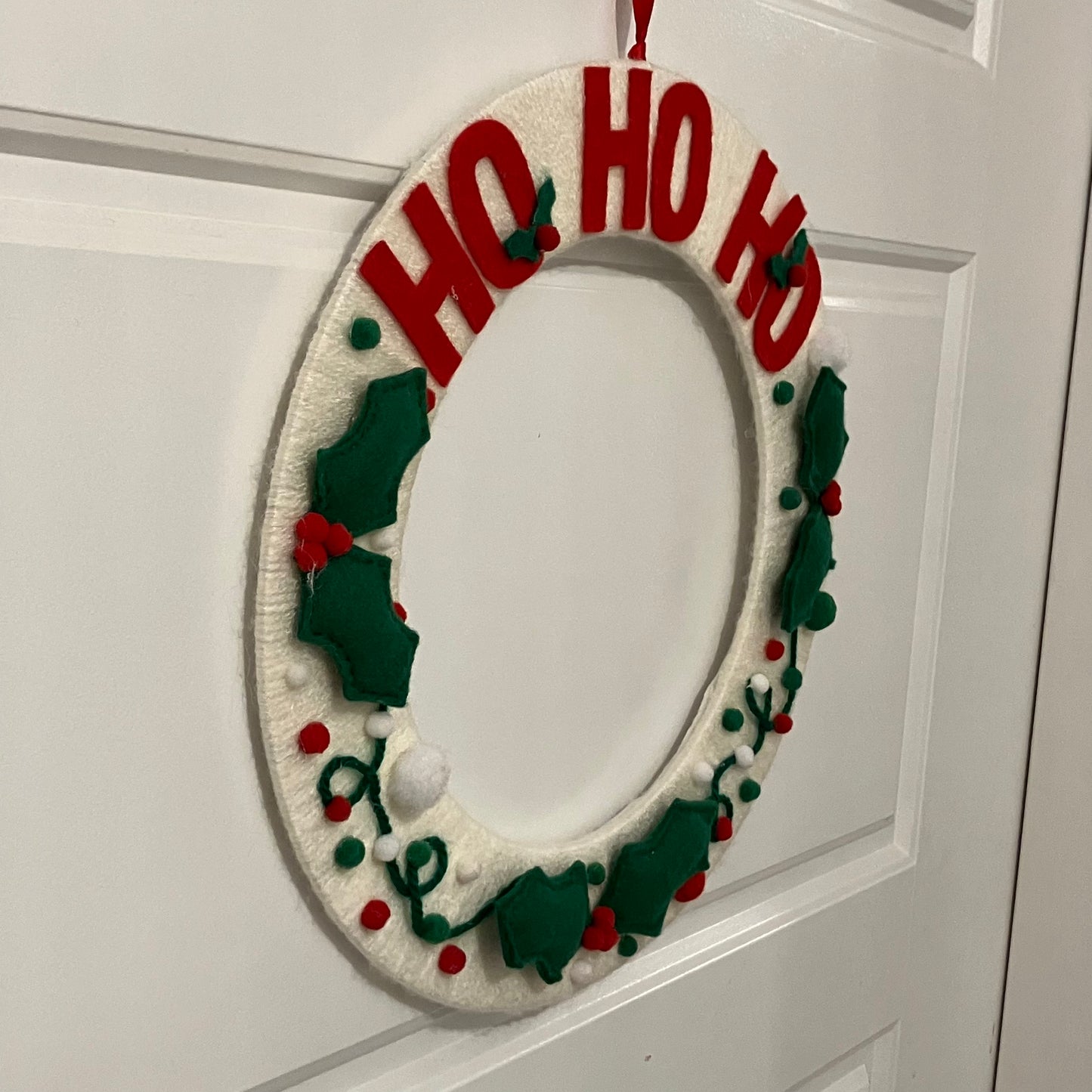 White knitted wreath with red "HO HO HO" and green holly decorations.