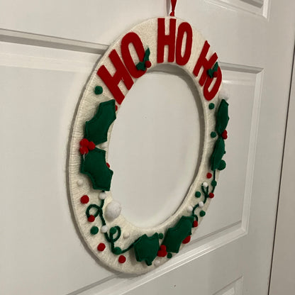 White knitted wreath with red "HO HO HO" and green holly decorations.