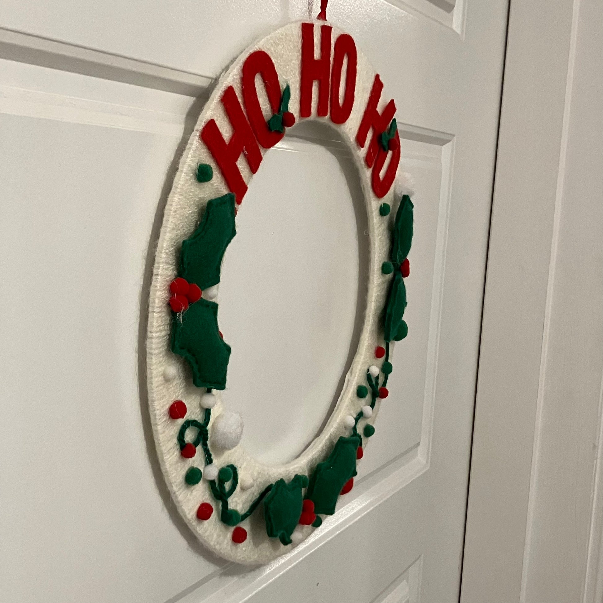White knitted wreath with red "HO HO HO" and green holly leaves.