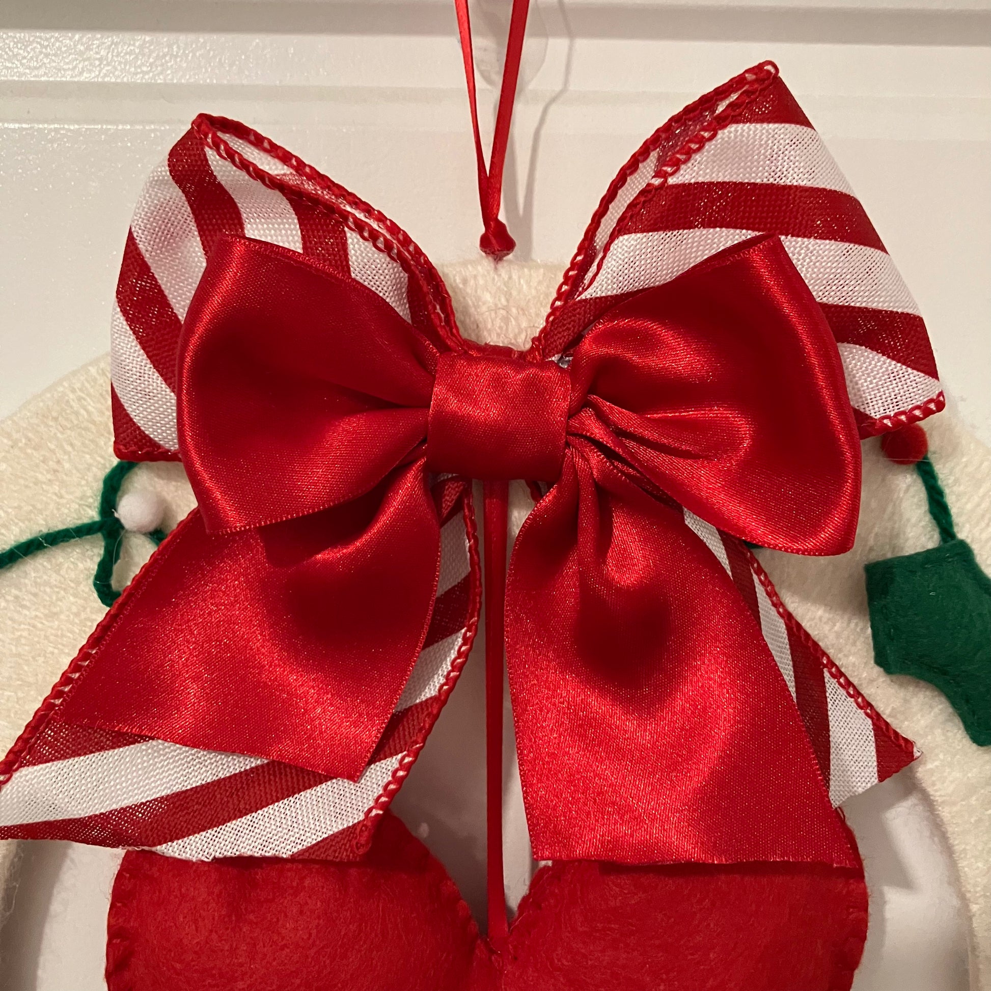 A festive red and white striped bow with a solid red satin bow on top, hanging from a red ribbon.