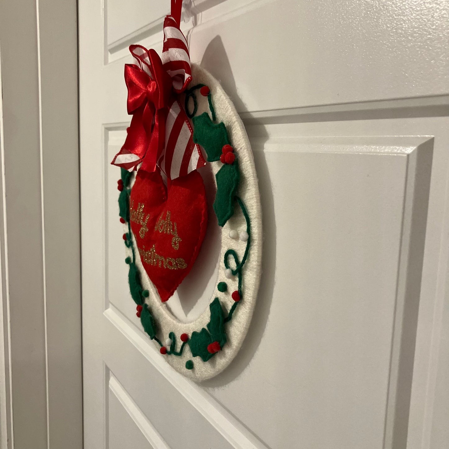 White Christmas wreath with red bow, candy cane, and heart-shaped ornament on a white door.