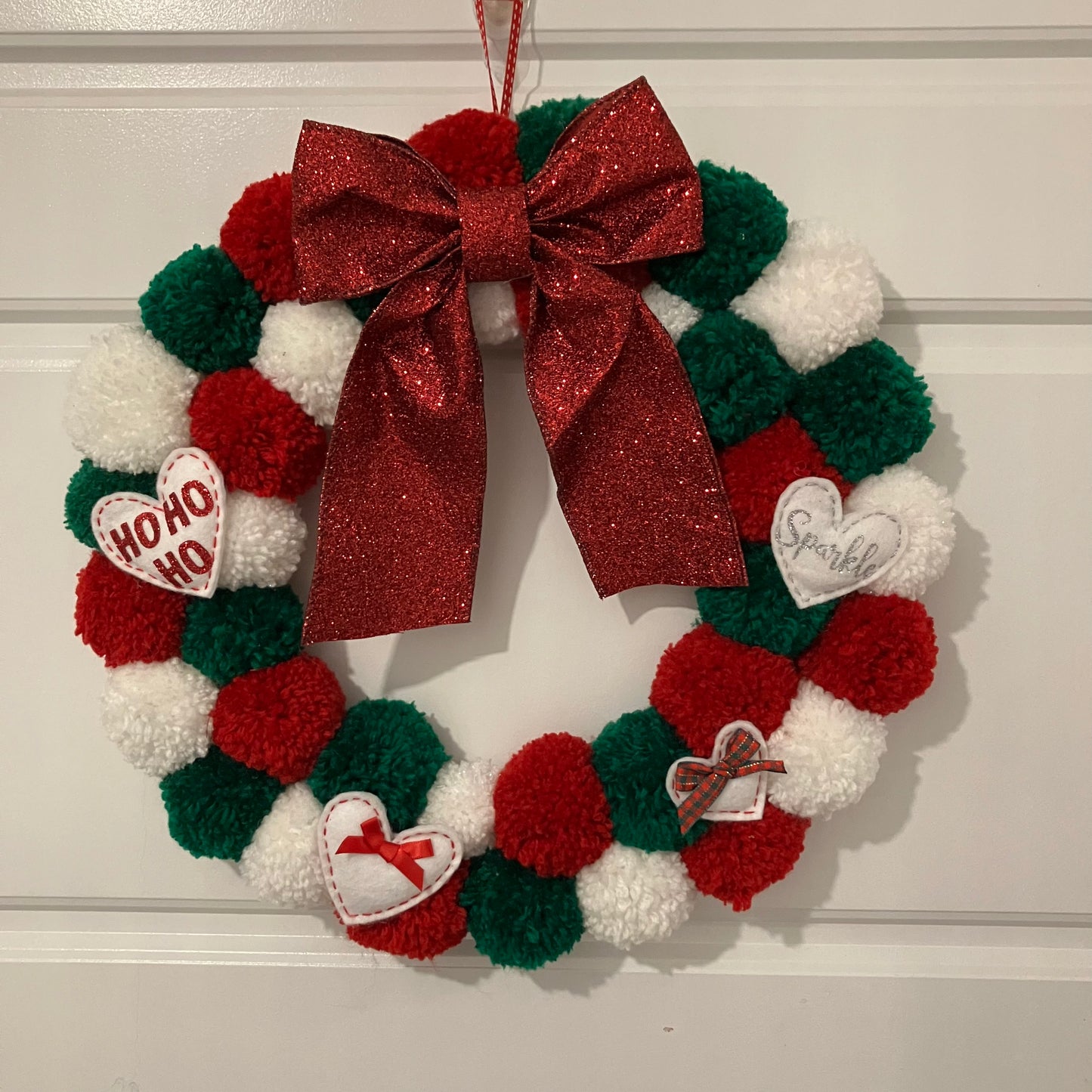Christmas wreath made of red, green, and white pom-poms with a large red glitter bow.
