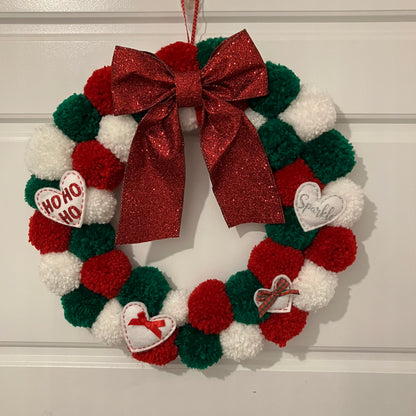 Christmas wreath made of red, green, and white pom-poms with a large red glitter bow.