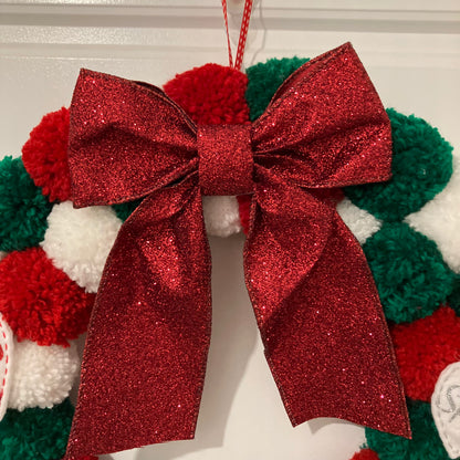 Red glitter bow on a Christmas wreath made of red, green, and white pom-poms.
