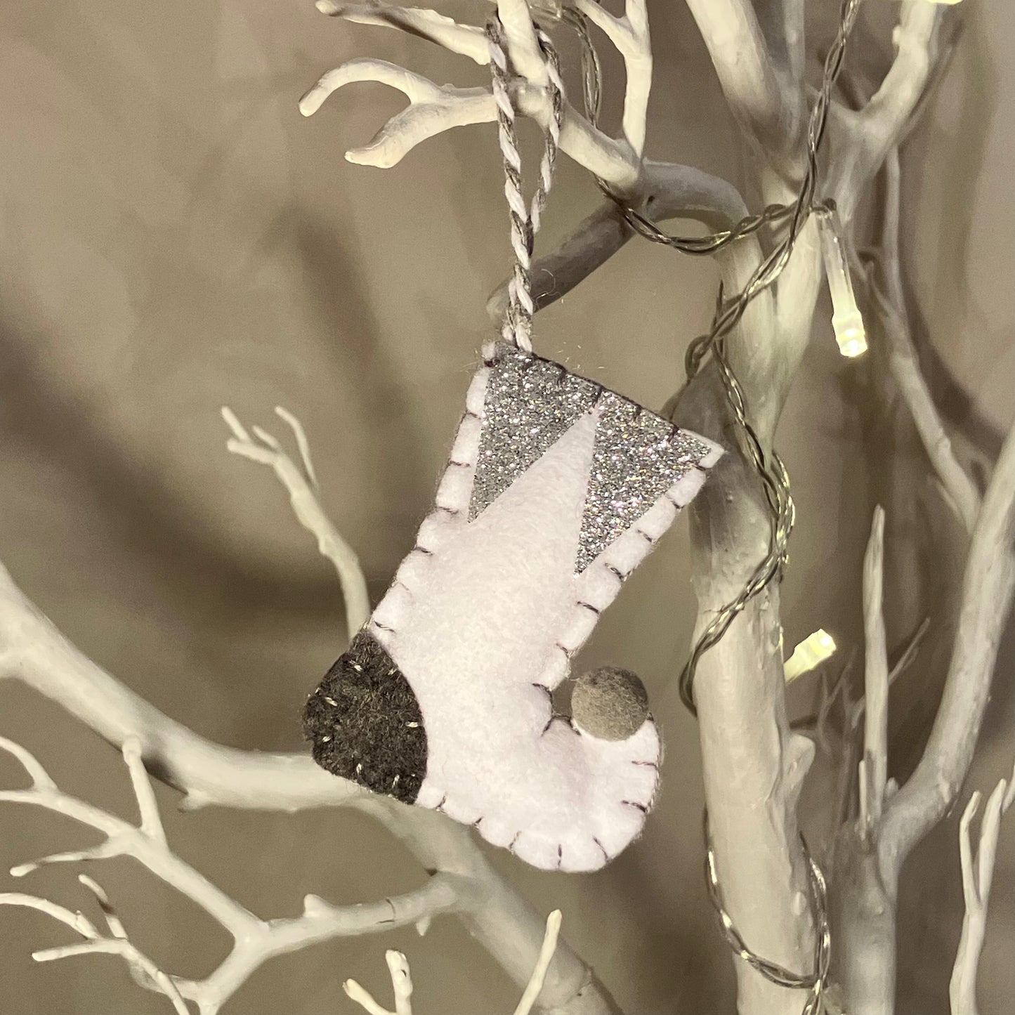 White felt stocking ornament with glitter accents hanging on a white branch.