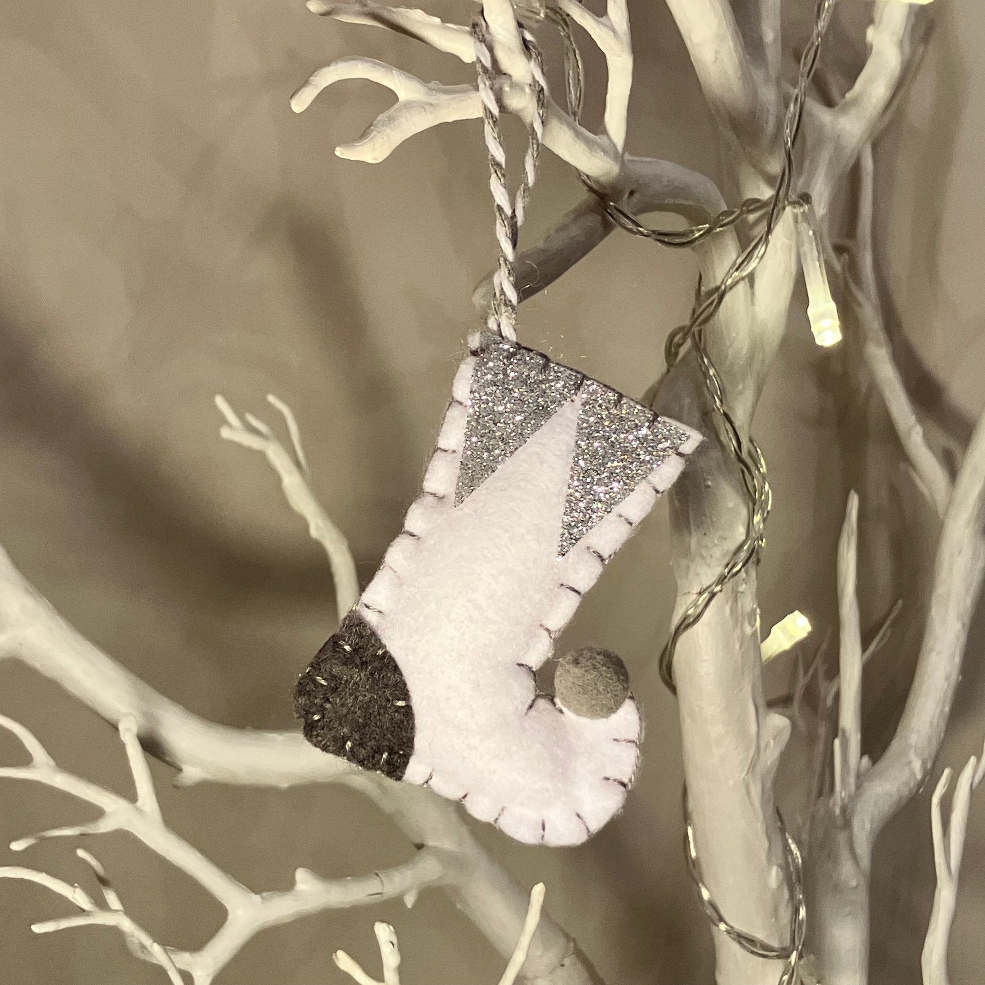 White felt stocking ornament with glitter accents hanging on a white branch.