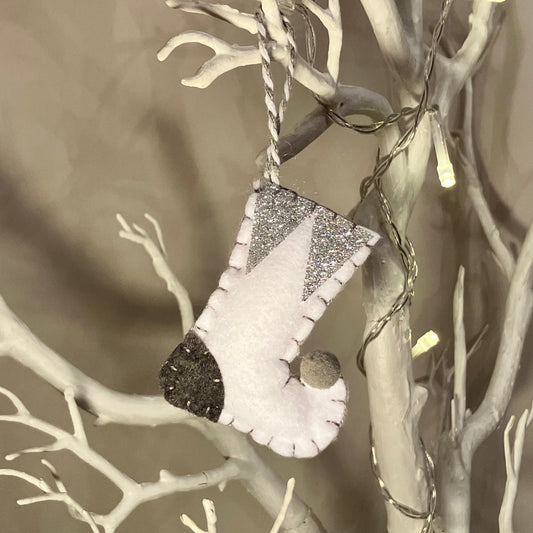 White felt stocking ornament with glitter accents hanging on a white branch.