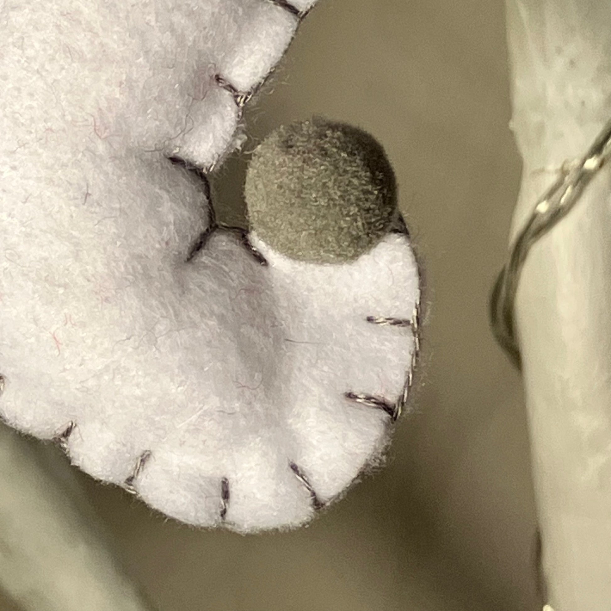 Close-up of a white felt ghost decoration with a small gray pom-pom nose and black stitching.