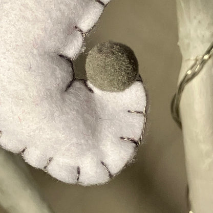 Close-up of a white felt ghost decoration with a small gray pom-pom nose and black stitching.