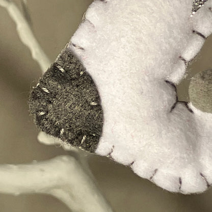 Close-up of a handmade white felt ornament with a dark gray tip and visible stitching.