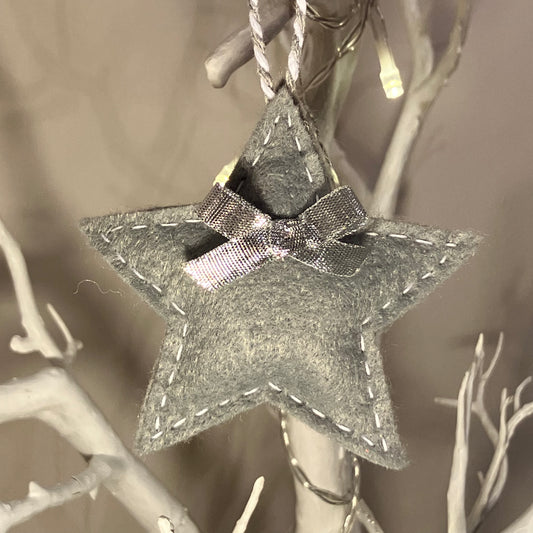 Grey felt star ornament with a silver bow, hanging from a white branch.