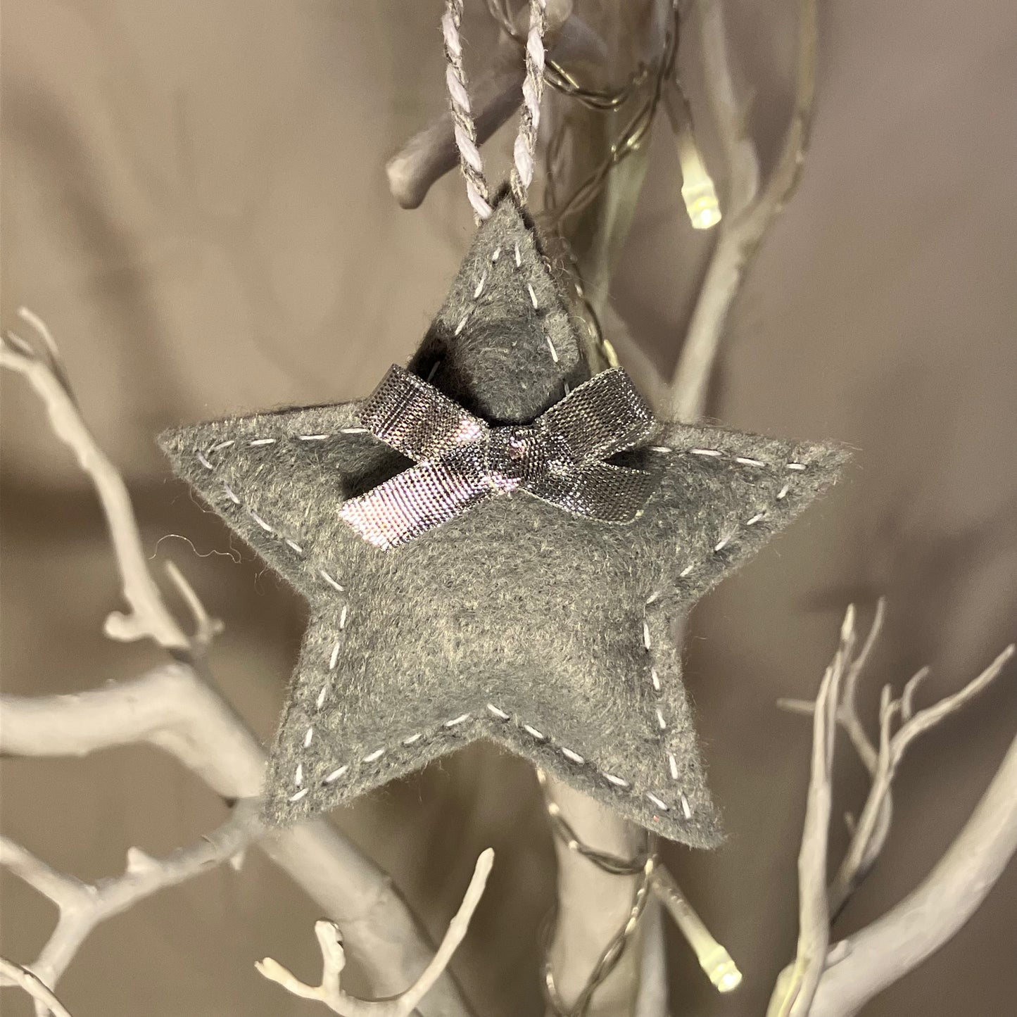 Handmade gray felt star ornament with a small bow, hanging from a white decorative branch.