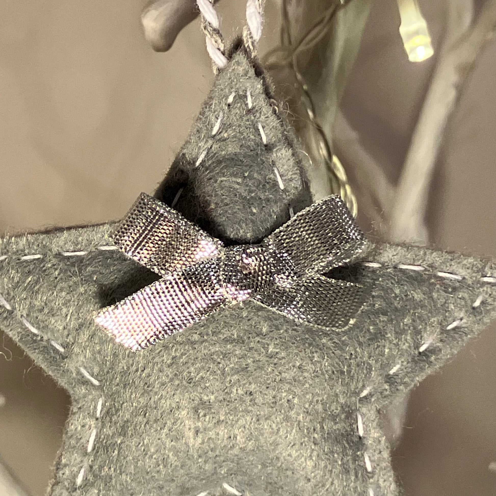 Handmade gray felt star ornament with white stitching and a silver bow.
