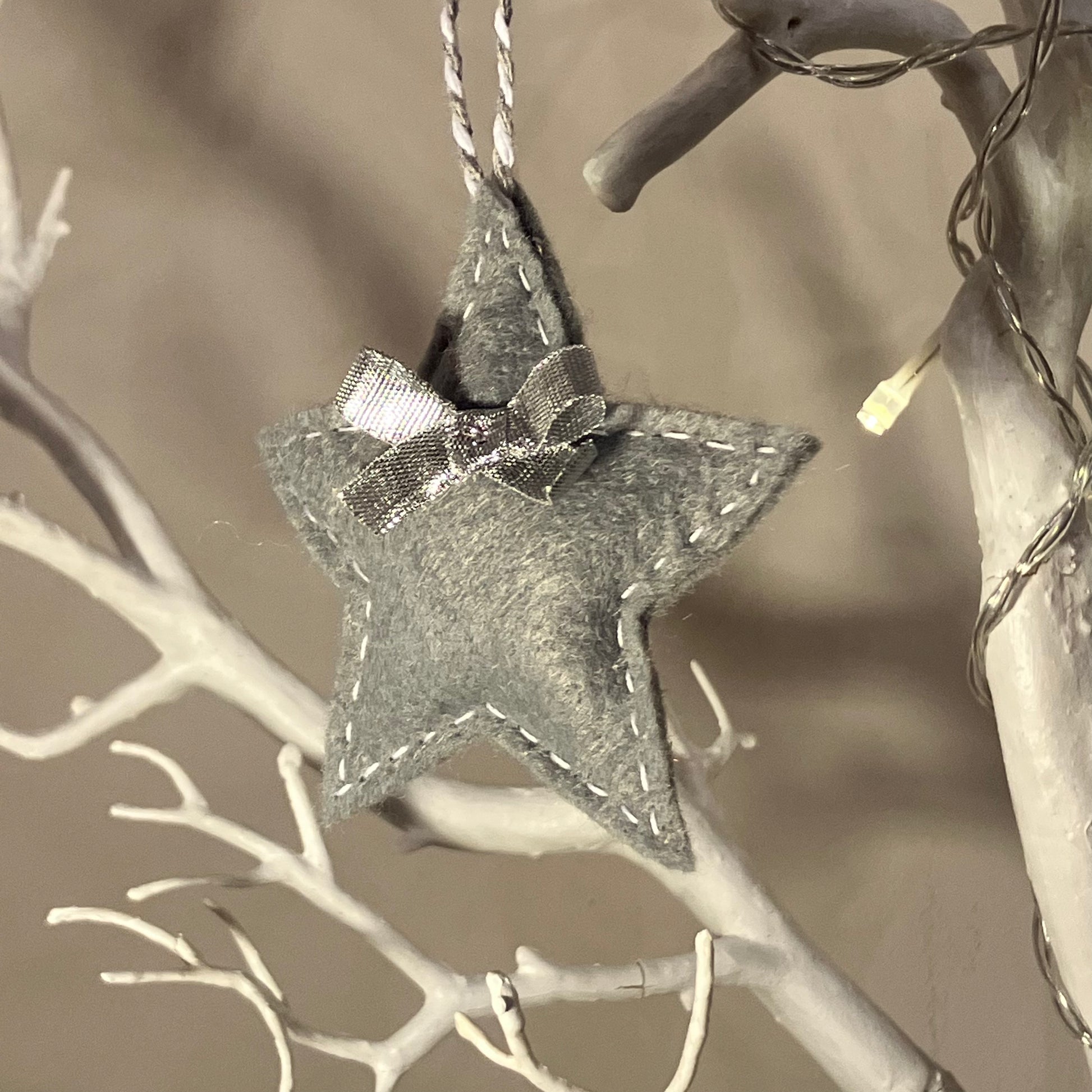 Handmade gray felt star ornament with white stitching and a small bow, hanging on a white branch.