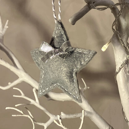 Handmade gray felt star ornament with white stitching and a small bow, hanging on a white branch.