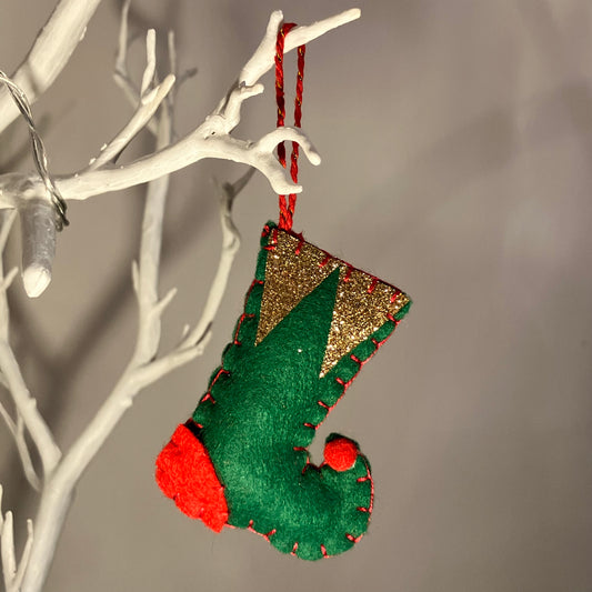Green felt Christmas stocking with gold glitter cuff and red accents, hanging on a white branch.
