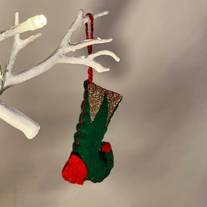 Green and red elf boot ornament with gold glitter hanging from a white branch.