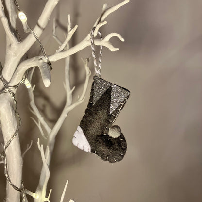 Handmade black felt Christmas stocking with white and silver accents hanging on a white branch.