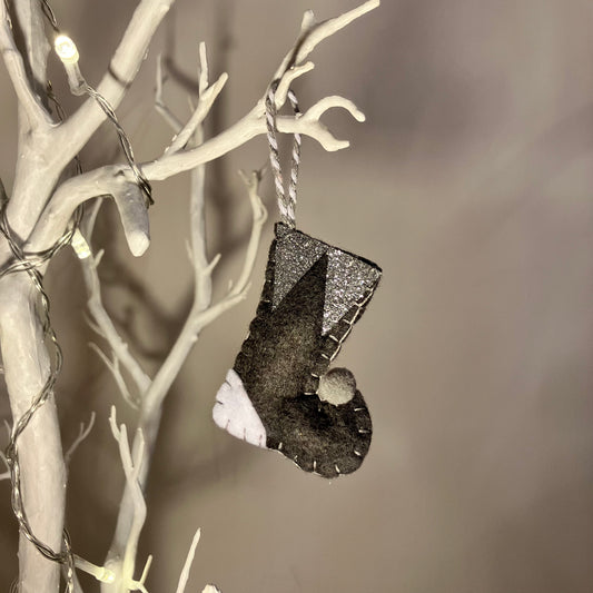 Handmade black felt Christmas stocking with white and silver accents hanging on a white branch.