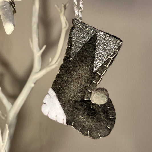 Handmade felt Christmas stocking ornament in black, white, and silver glitter, hanging from a white branch.