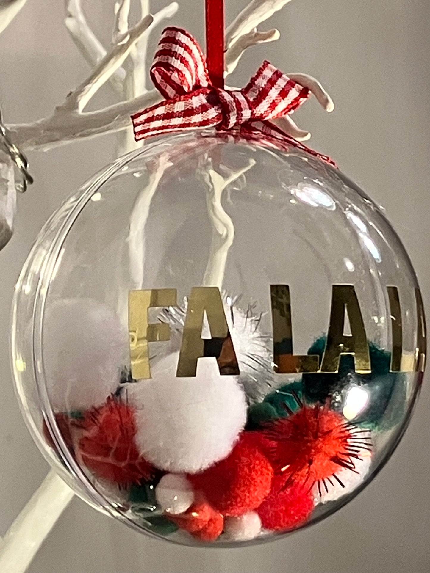 Clear ornament with red and white bow, pom-poms, and "FA LA LA!" in gold letters.