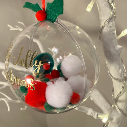 Clear Christmas bauble with "Jolly Christmas" text, filled with red, white, and green pom-poms.